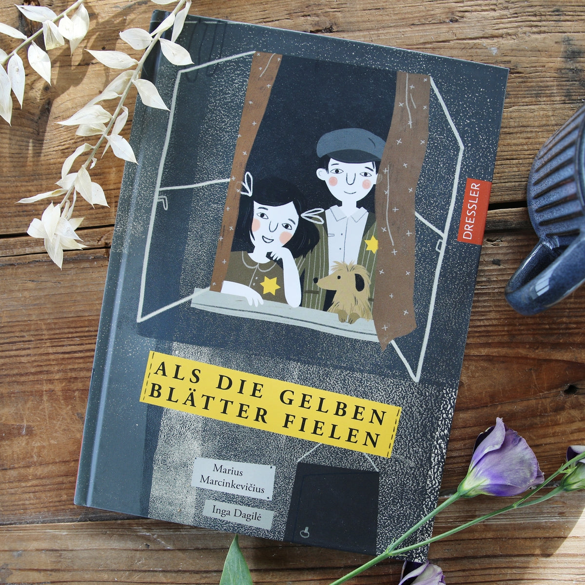 Buchcover von „Als die gelben Blätter fielen“. Zwei Kinder, ein Mädchen und ein Junge, blicken mit einem Hund aus einem Fenster. 