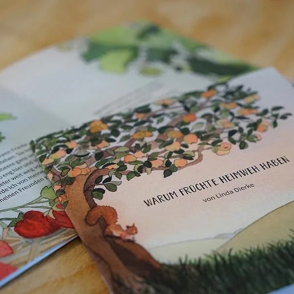 Produktfoto des Kinderbuchs "Warum Früchte Heimweh haben" von Linda Dierke: Cover mit Apfelbaum und Eichhörnchen liegt leicht geöffnet auf einem Tisch.